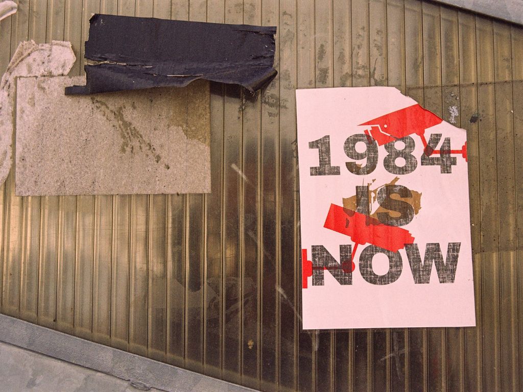 Eine Blechwand, daran ein Plakat mit der Aufschrift: 1984 is Now.