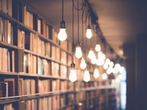 Mehrere leuchtende Glühbirnen hängen vor einem Bücherregal von der Decke
